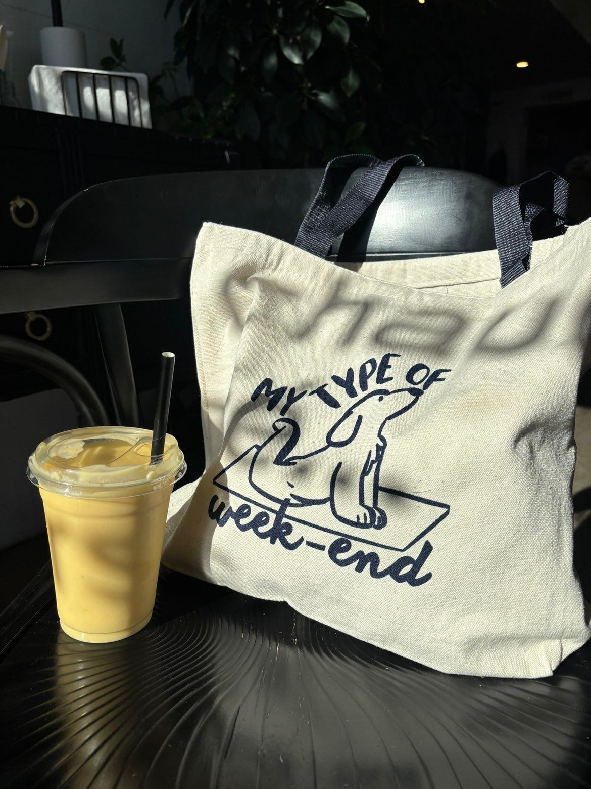 Tote bag en toile beige avec une illustration de chien faisant du yoga et l'inscription "My type of week-end", posé à côté d'un smoothie.